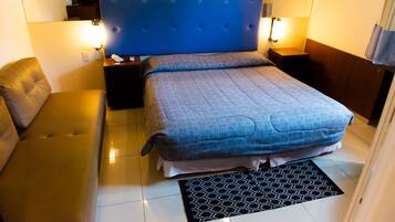 Une chambre d’hôtel avec un grand lit, un canapé, une table de chevet et une lampe.