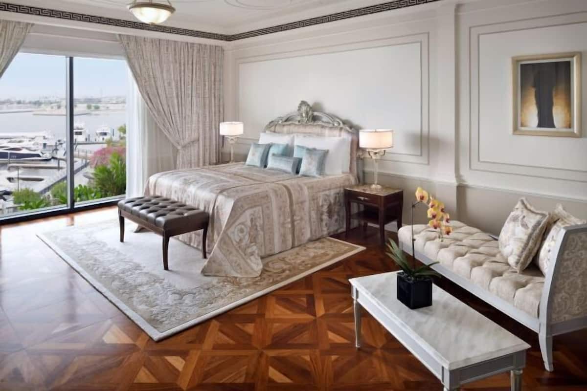 Ein Schlafzimmer mit einem großen Bett, einer Couch, einem kleinen Tisch, einem Nachttisch und Blick auf den Hafen.