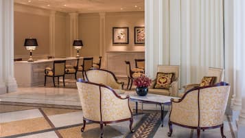 Uma sala de jantar formal com piso de mármore, cadeiras estampadas, uma mesa central com um vaso e uma lareira ao fundo.
