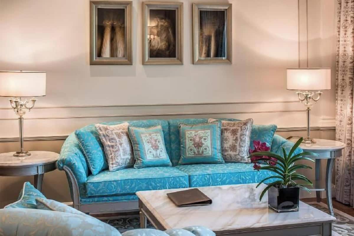 Ein Zimmer mit einem blauen, gemusterten Sofa, einem kleinen Tisch mit einer Pflanze und drei gerahmten Kunstwerken an der Wand.