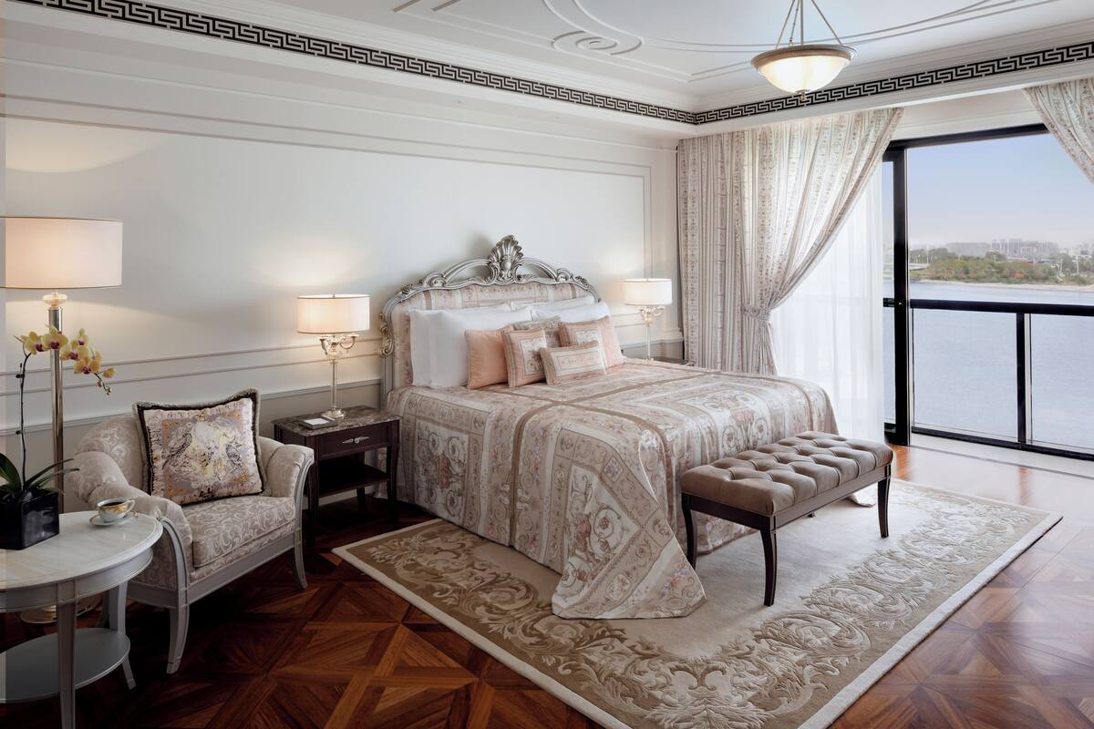 Ein Schlafzimmer mit einem großen Bett, einem Sessel, einem Nachttisch und Blick ins Freie.