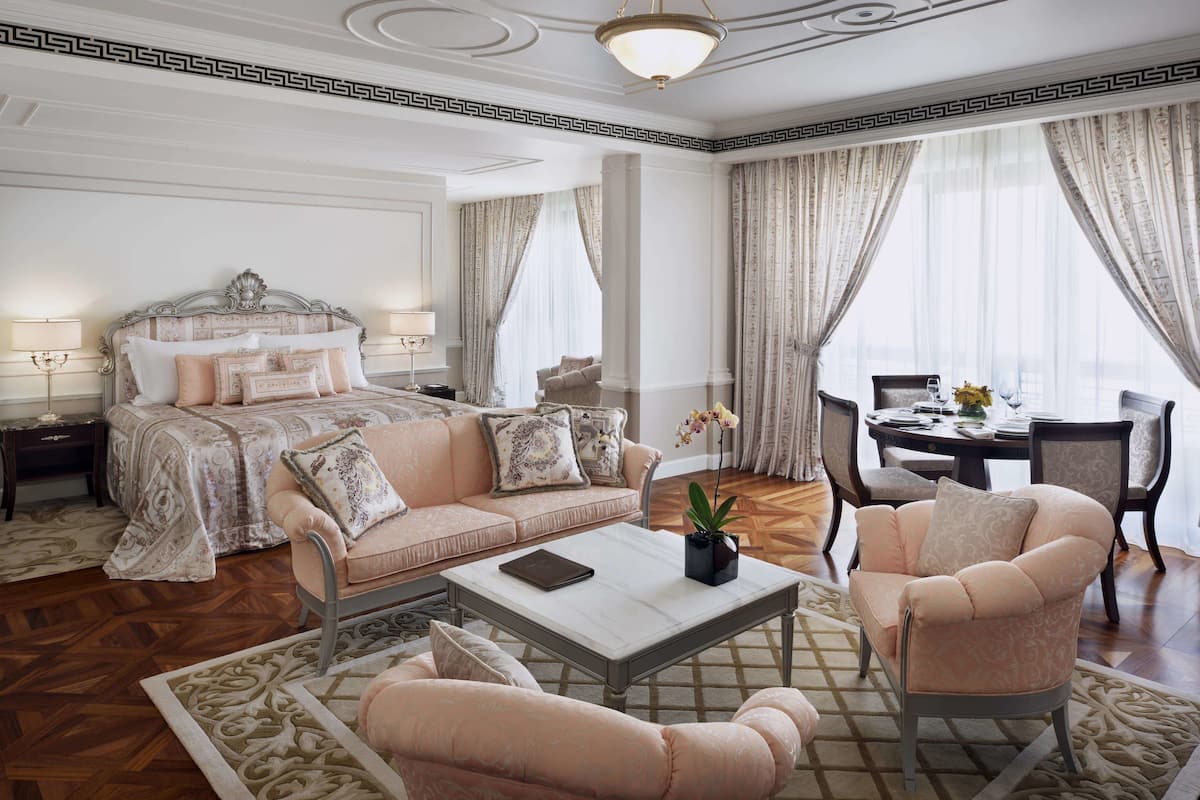 Ein geräumiges Schlafzimmer mit einem großen Bett, einer Sitzecke mit einer Couch und Sesseln sowie einem Esstisch mit Stühlen.