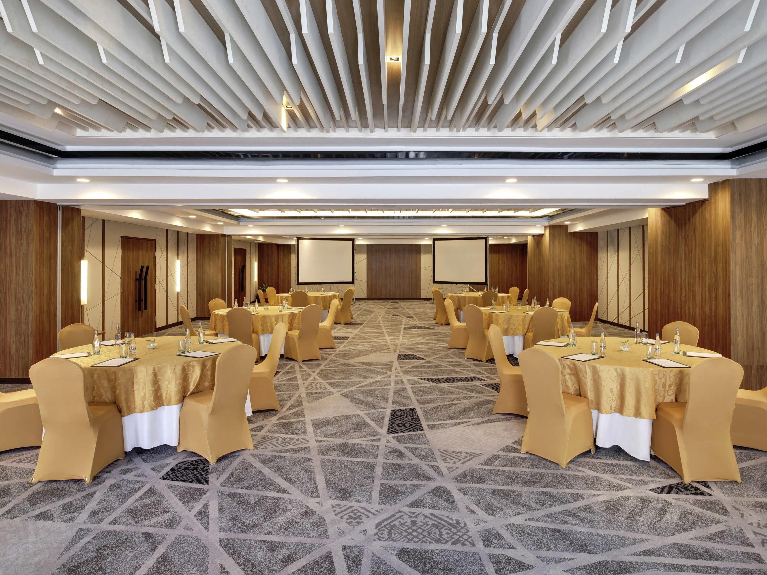 A conference room with multiple tables, chairs, and a large screen.