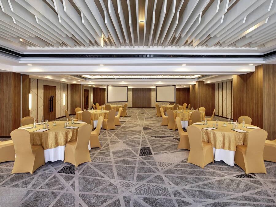 A conference room with multiple tables, chairs, and a large screen.