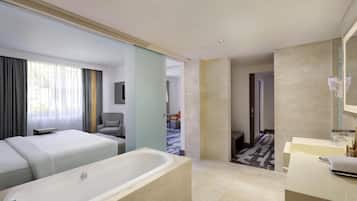 Una habitación de hotel moderna con una cama grande, una bañera y un baño separado con tocador y espejo.