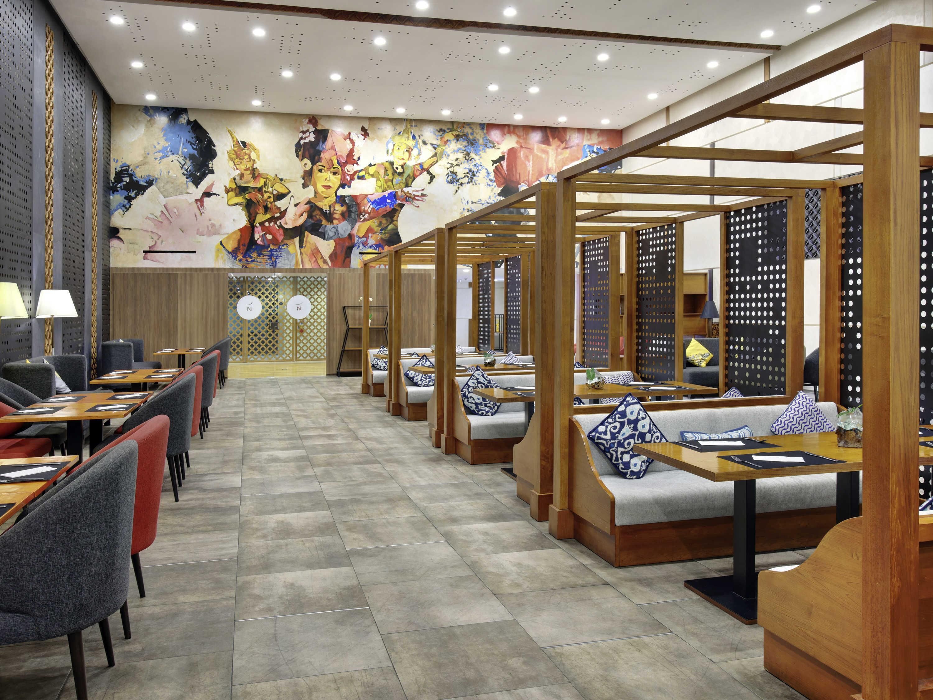 A modern restaurant with booths and tables, a colorful mural on the wall, and a wooden ceiling structure.