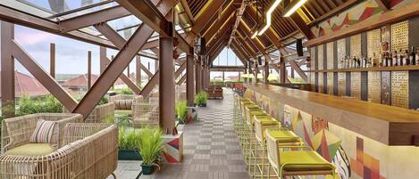A spacious bar area with high ceilings and exposed beams, featuring wicker furniture and a long counter with bar stools.
