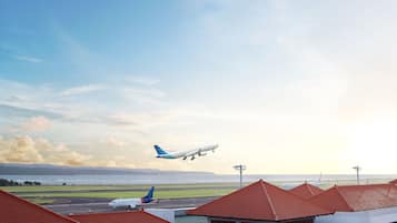 An airport with a runway, buildings with red roofs, and airplanes in the sky.
