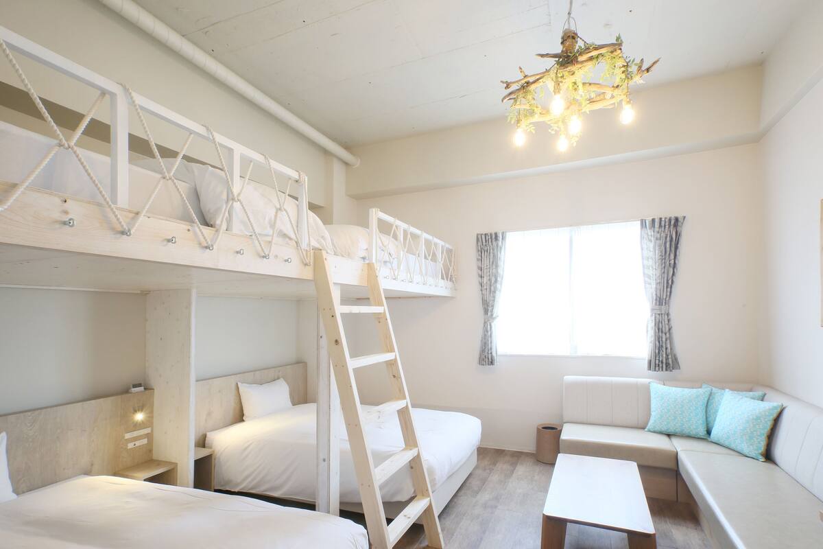 Ein Zimmer mit Etagenbetten, einer Klapptreppe, einer Couch, einem Tisch und einem Fenster mit Vorhängen.