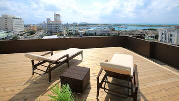 A wooden deck with two wicker lounge chairs and a small table, overlooking a cityscape and a body of water.