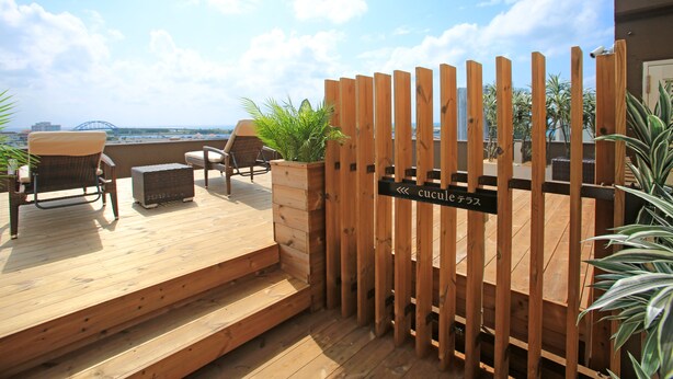 Une terrasse en bois avec des sièges d’extérieur, une clôture en bois et une enseigne avec des caractères japonais.