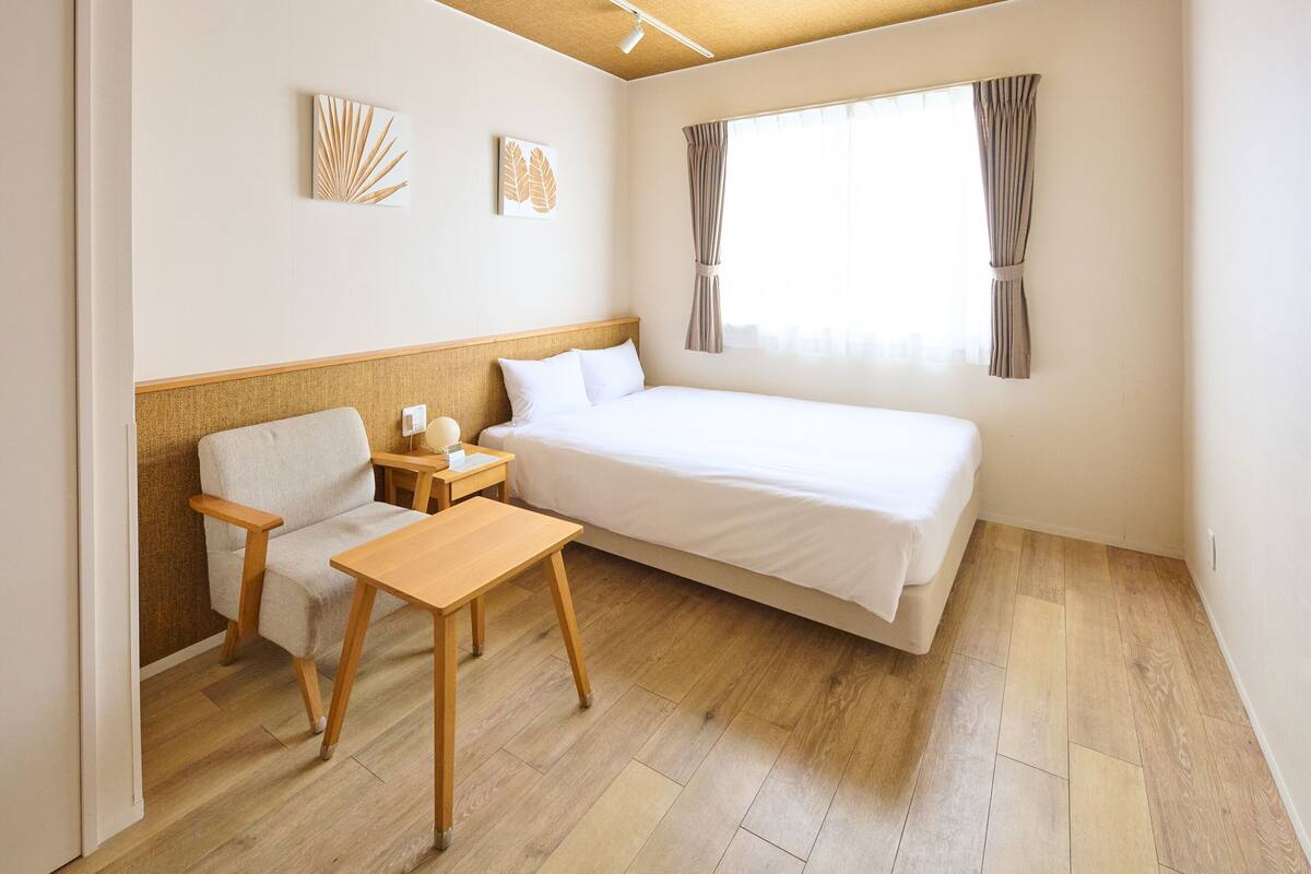 Ein Hotelzimmer mit Bett, Sessel, kleinem Tisch, Nachttisch und zwei an der Wand befestigten Kunstwerken.