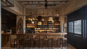 Un espace bar avec des tabourets en bois, un comptoir et des étagères remplies de bouteilles et de verres.