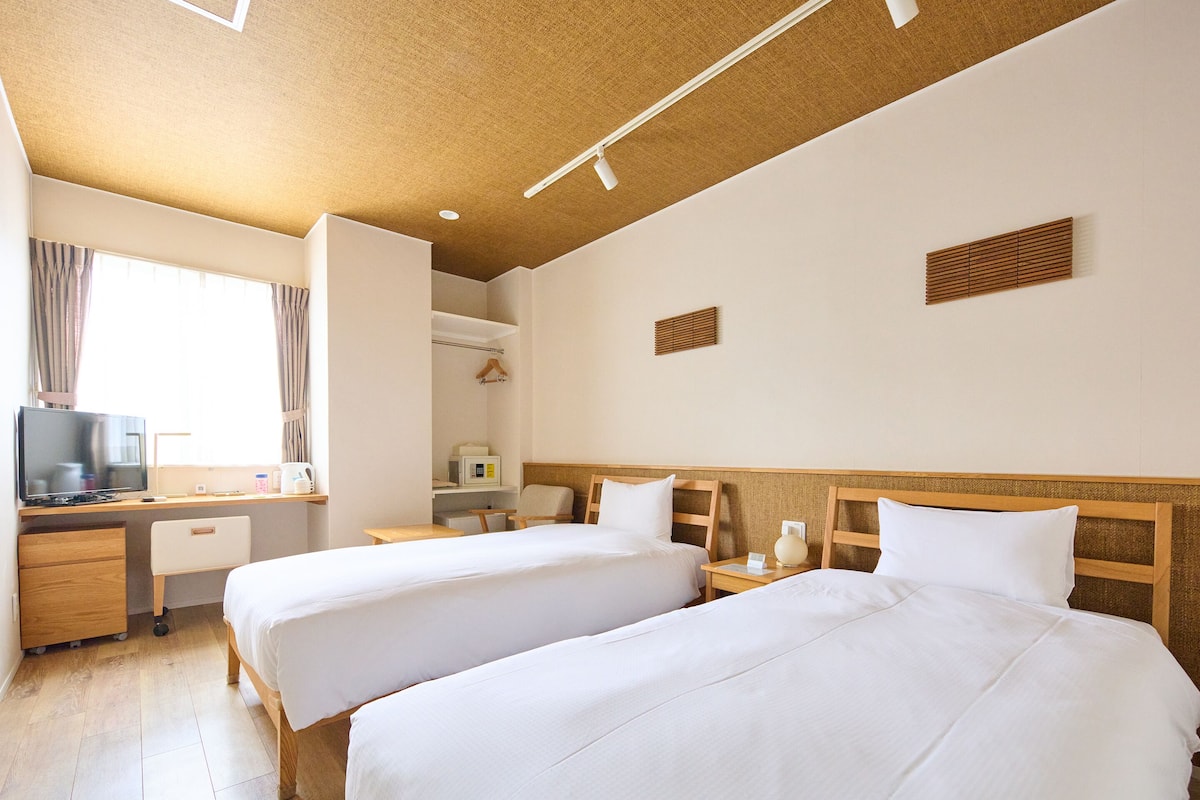 Ein Hotelzimmer mit zwei Betten, einem Schreibtisch, einem Fernseher, einer Mikrowelle und einem kleinen Tisch.