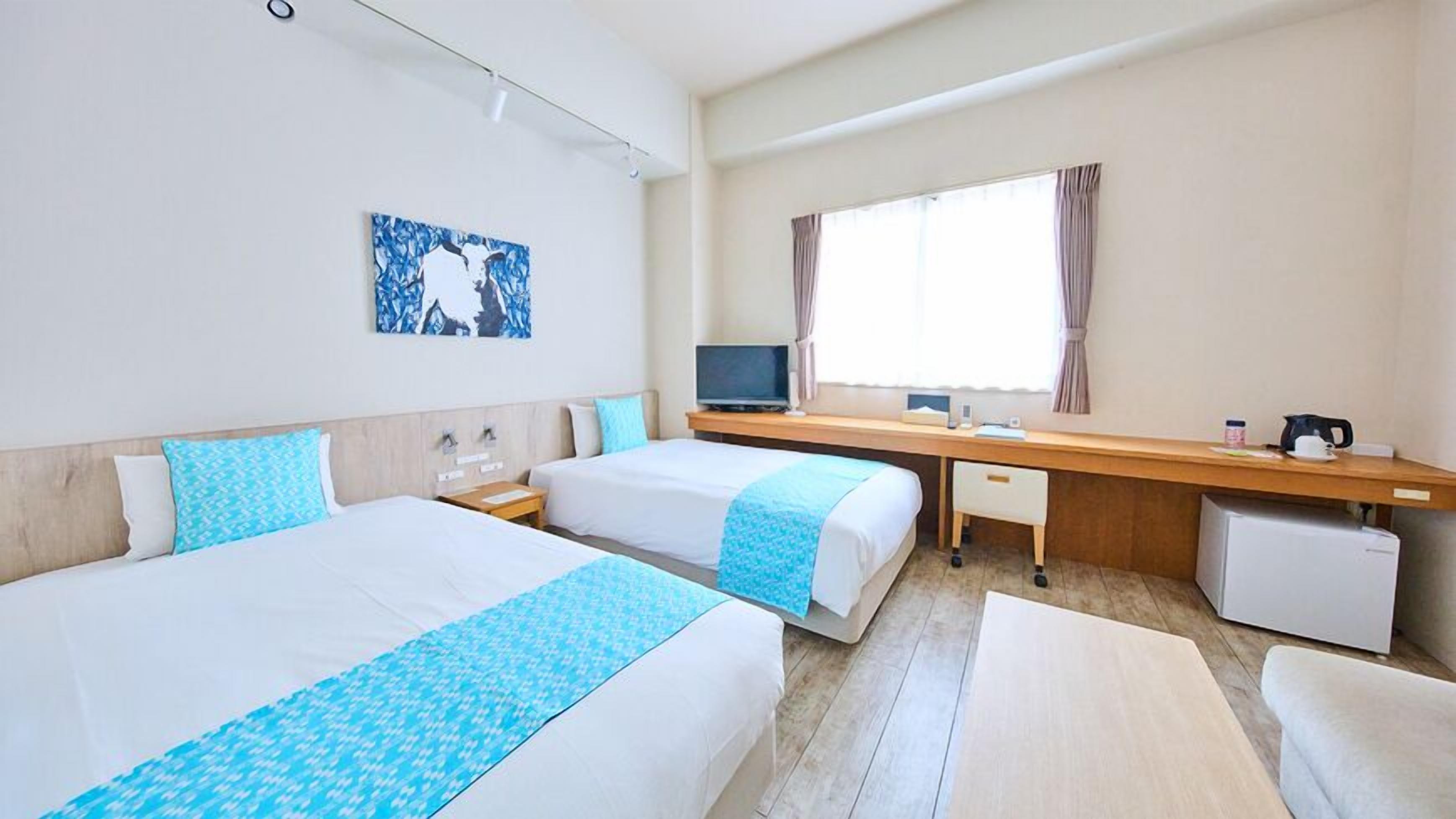 Quarto de hotel com duas camas, uma escrivaninha, televisão e janela com cortinas.