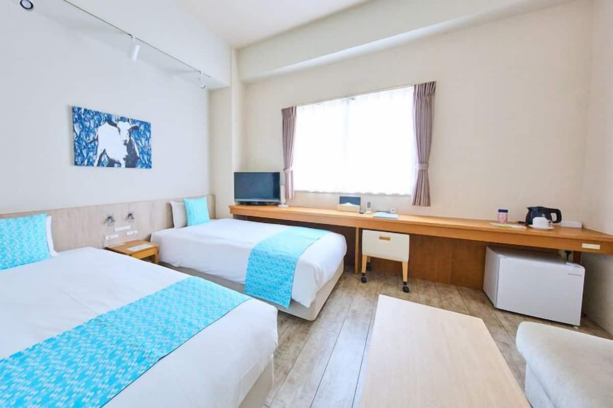 Ein Hotelzimmer mit zwei Betten, einem Schreibtisch, einem Fernseher und einem fenster mit Vorhängen.