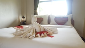 Cama bem arrumada com toalha dobrada em formato de cisne, travesseiro vermelho e branco, e uma luminária de mesa pequena.