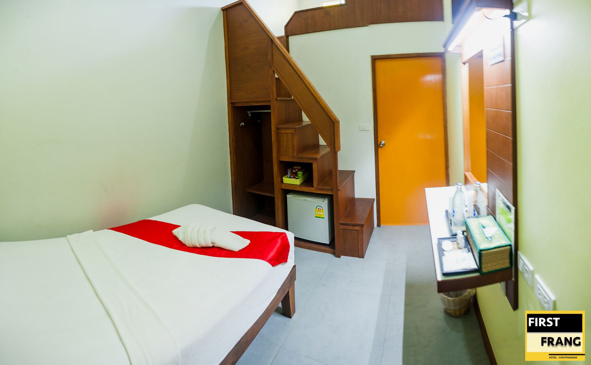 Une chambre d’hôtel comprenant un lit, un petit bureau avec une chaise, une armoire en bois, un mini-réfrigérateur et une porte donnant sur une autre pièce.