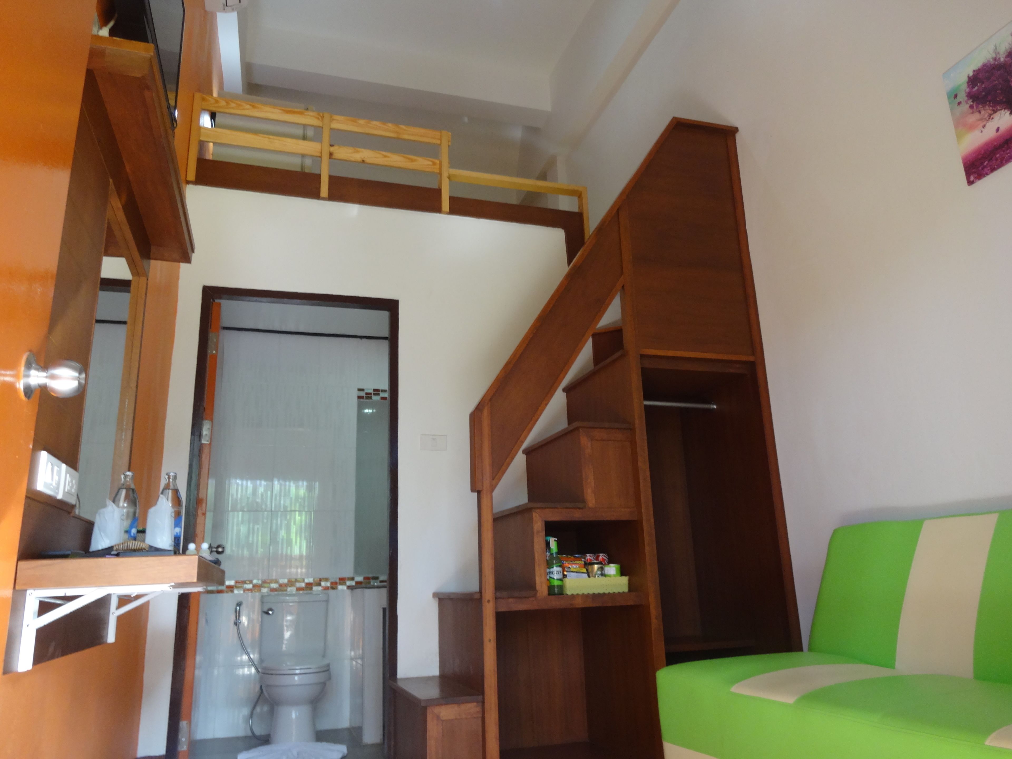 A compact living space with a bunk bed, a green sofa, wooden shelves, and a bathroom with a toilet and shower.