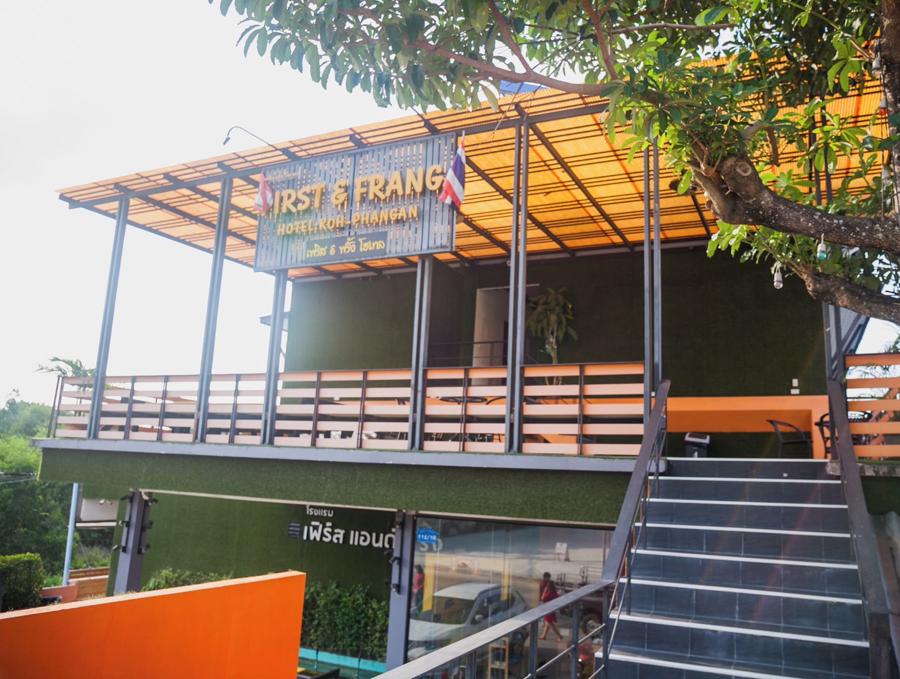 A hotel named 'First & Frang' with a modern design, featuring a covered outdoor area and a staircase leading to the entrance.