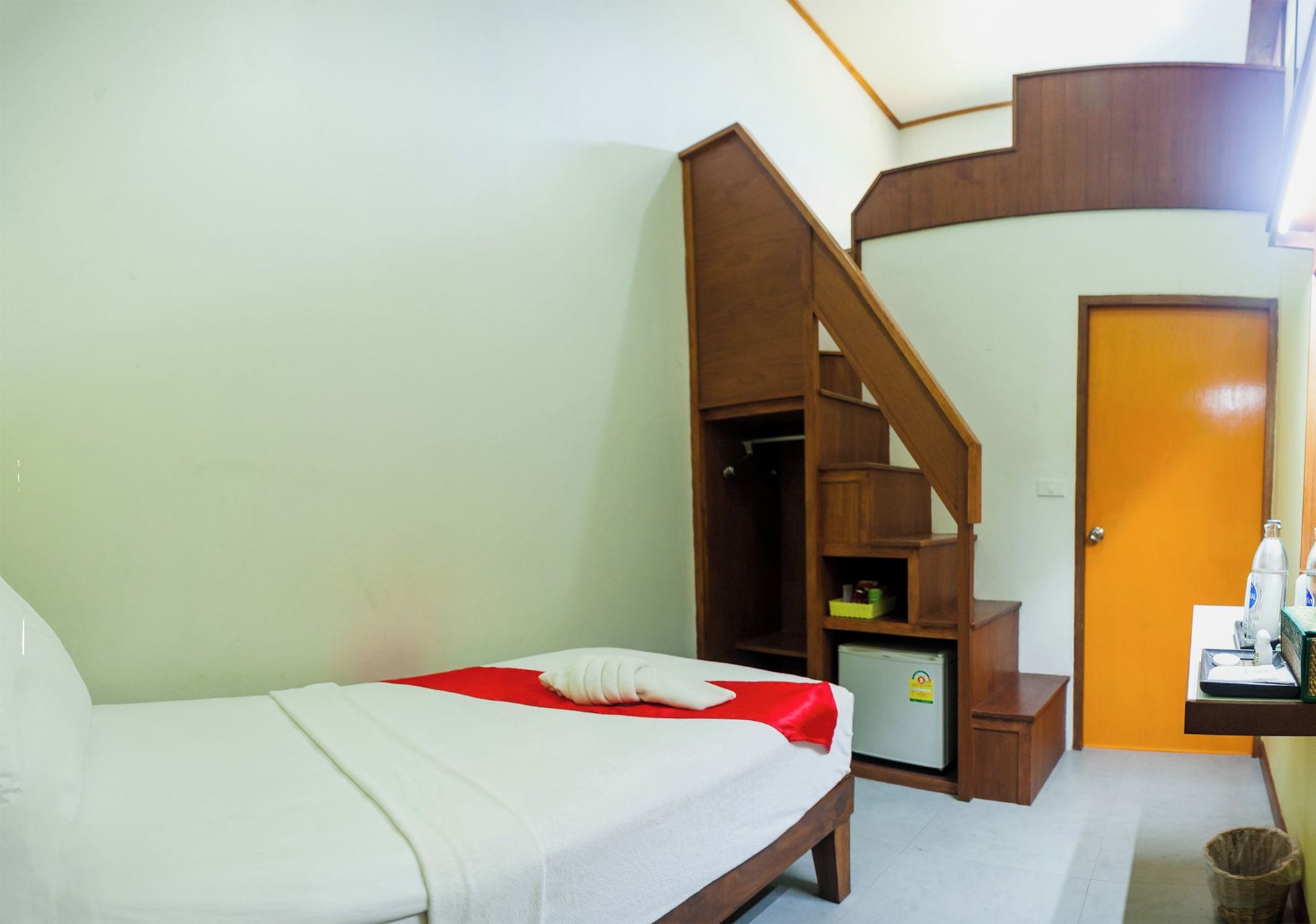Ein Hotelzimmer mit einem Bett, einem kleinen Schreibtisch mit Computer, einem Kühlschrank und einer Holztreppe.