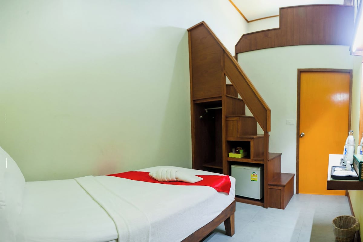 A hotel room with a bed, a small desk with a computer, a refrigerator, and a wooden staircase.