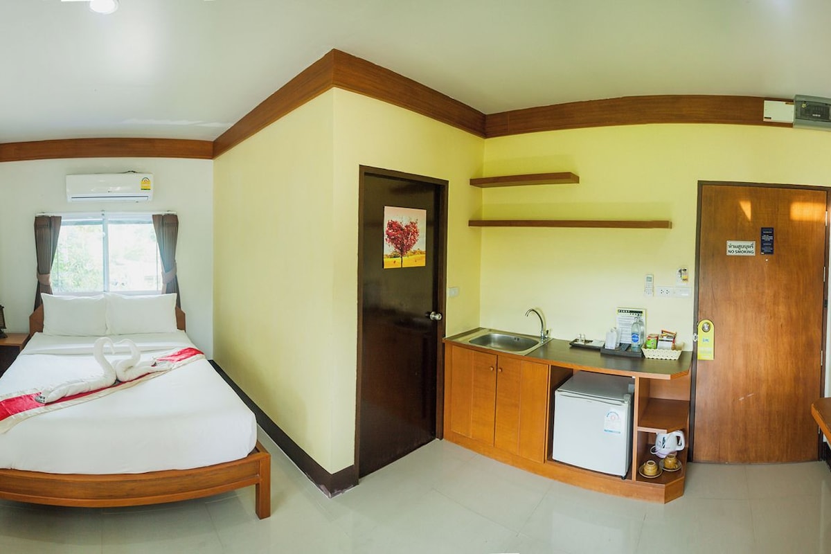 A hotel room with a bed, a small kitchenette, a bathroom, and a window with curtains.