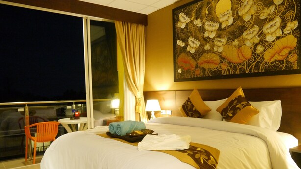 A hotel room with a large bed, a nightstand with a lamp, a window with curtains, and a painting on the wall. - Golden Moon Aonang (Krabi)