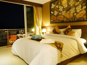 A hotel room with a large bed, a nightstand with a lamp, a window with curtains, and a painting on the wall. - Golden Moon Aonang (Krabi)