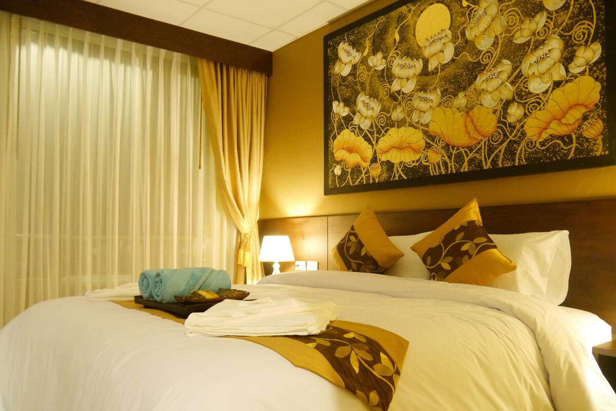 Una habitación de hotel con una cama grande, ropa de cama blanca, una toalla azul y un cuadro de flores en la pared.