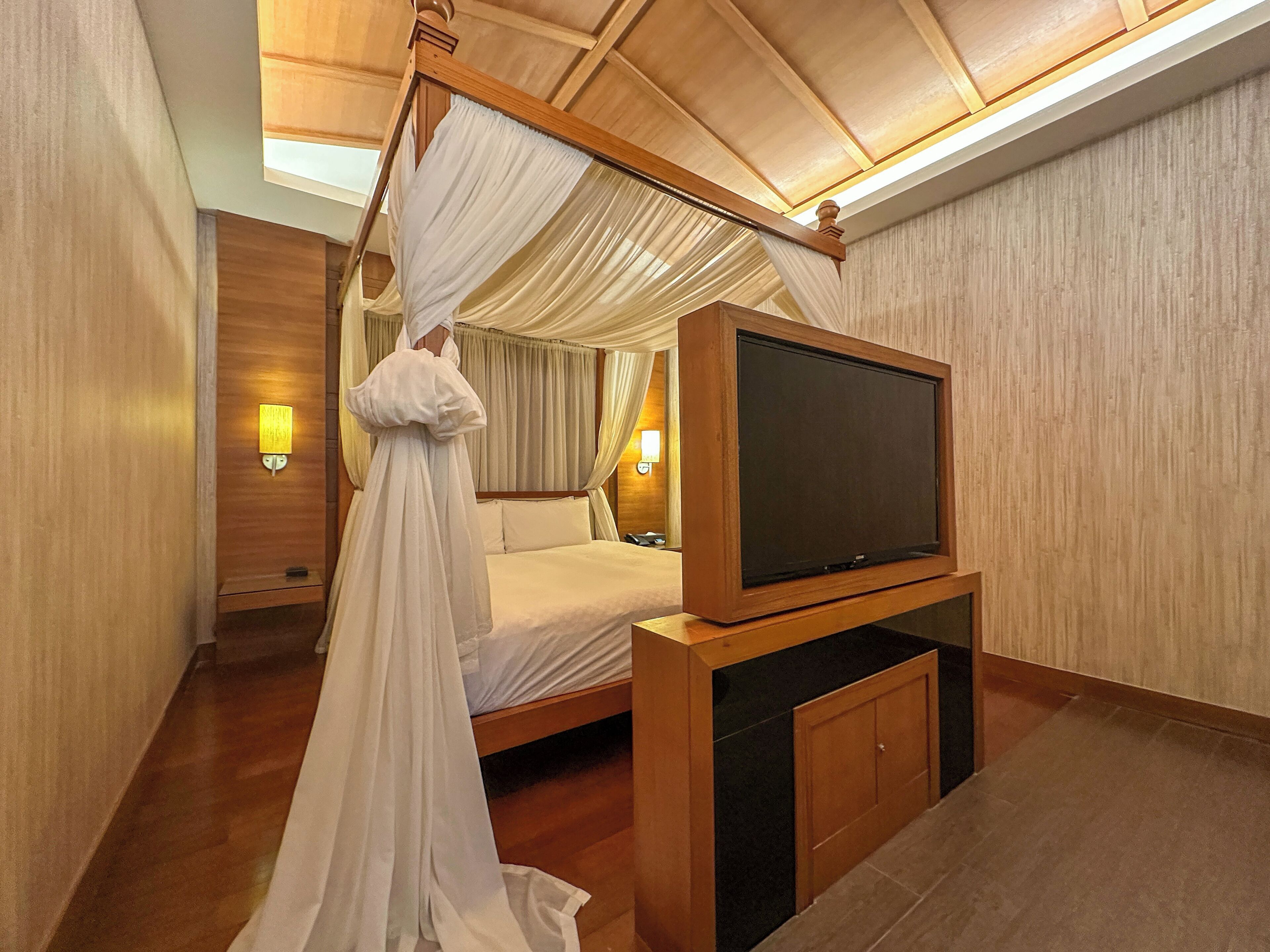 Una camera da letto con un letto a baldacchino, una televisione su un mobile in legno e un comodino.