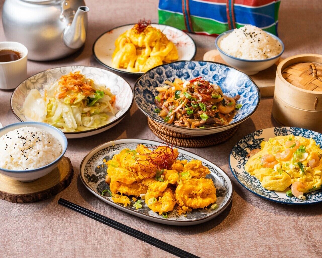 A variety of dishes including rice, fried items, and a teapot.