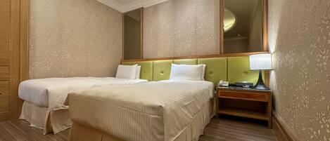 A hotel room with two beds, a nightstand with a lamp, and a large mirror on the wall.