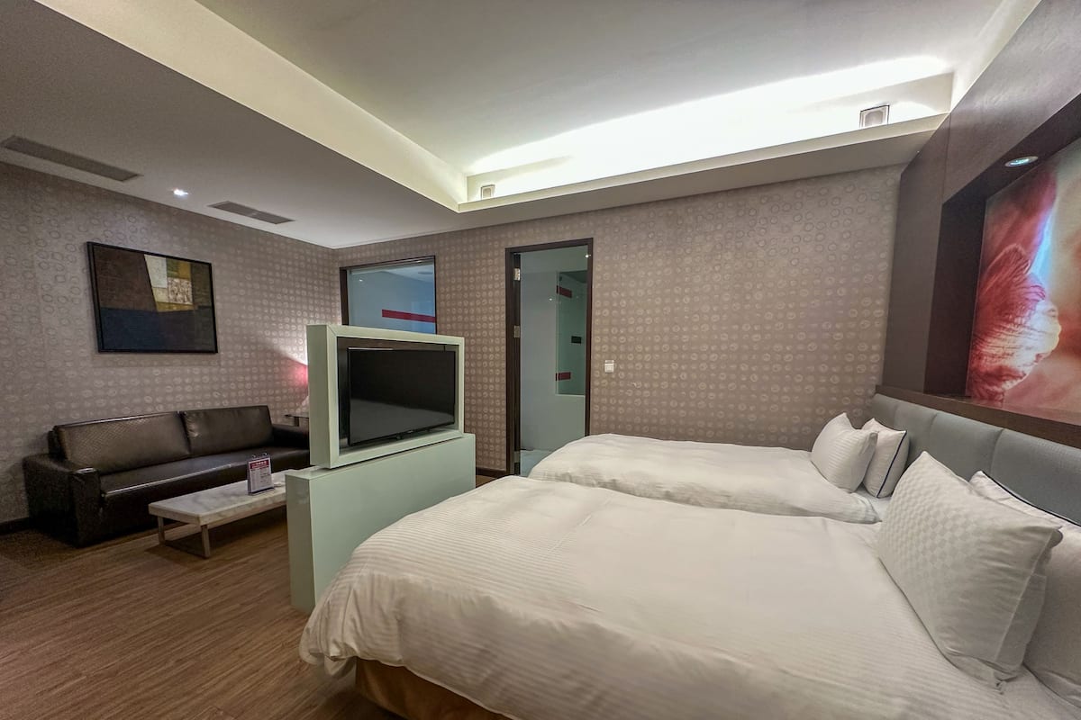 A hotel room with two beds, a TV on a stand, a sofa, and a small table.