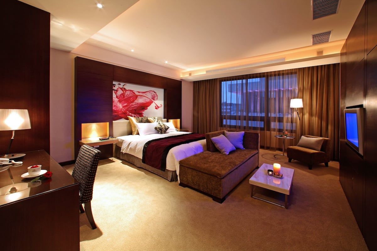 A hotel room with a bed, a sofa, a desk, a TV, and a large window with curtains.
