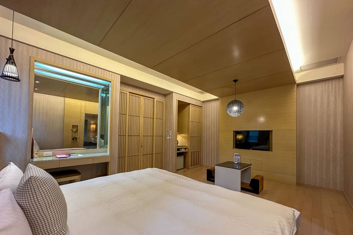 A modern hotel room with a large bed, a desk, a TV, and a wardrobe.