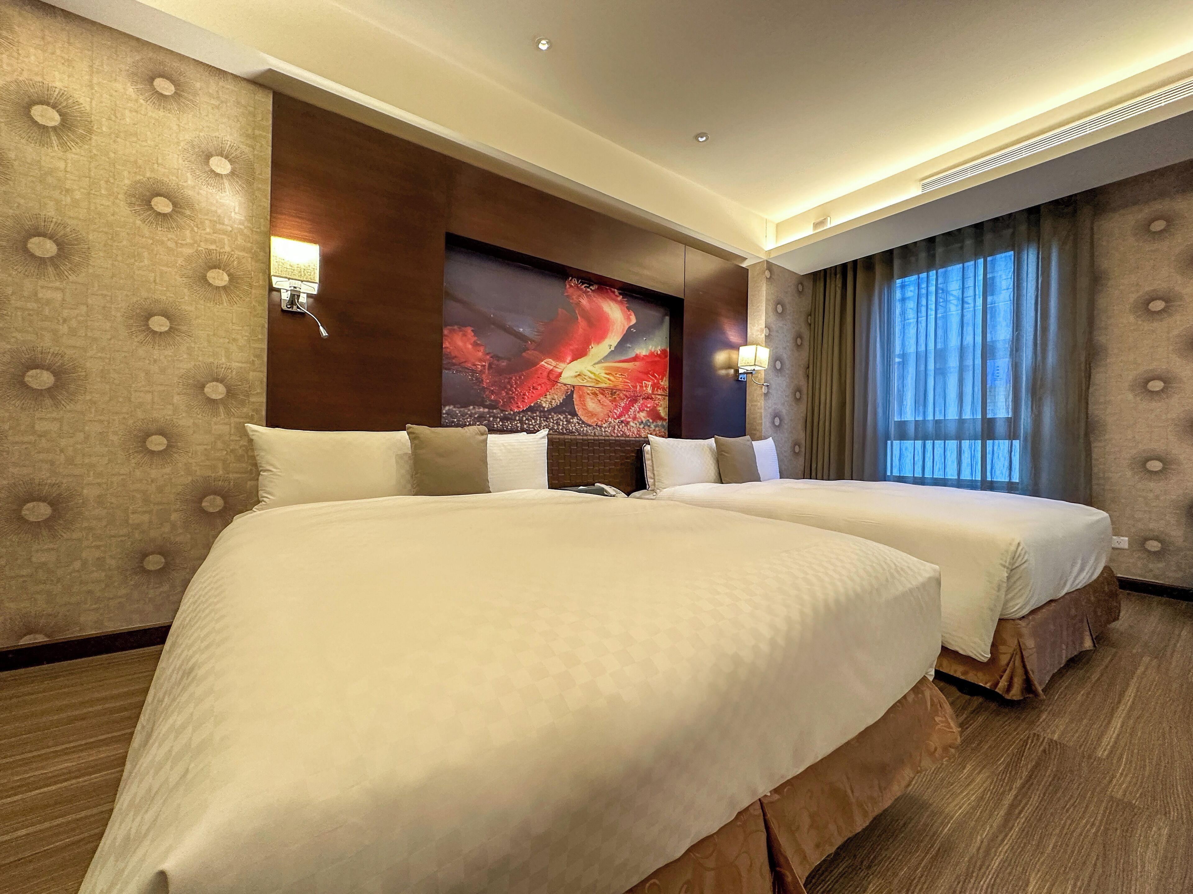 Habitación de hotel con dos camas, una obra de arte grande en la pared y una ventana con cortinas.