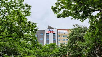 A hotel building with multiple floors, surrounded by lush green trees.