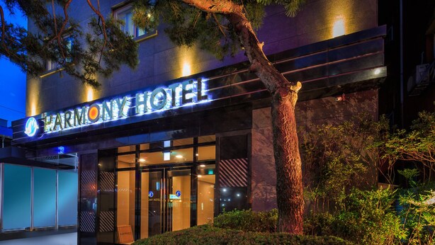 The exterior of the Harmony Hotel with a prominent illuminated sign, a large tree in front, and a well-lit entrance. - Harmony Hotel (Seoul)