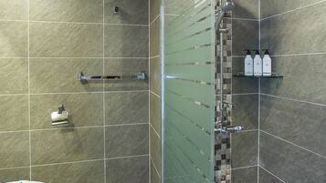 A modern bathroom with a glass-enclosed shower, a toilet, and a shelf with toiletries.