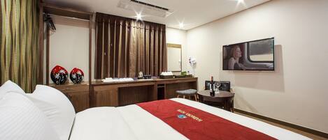 A hotel room with a bed, a desk, a chair, a TV, and a minibar.