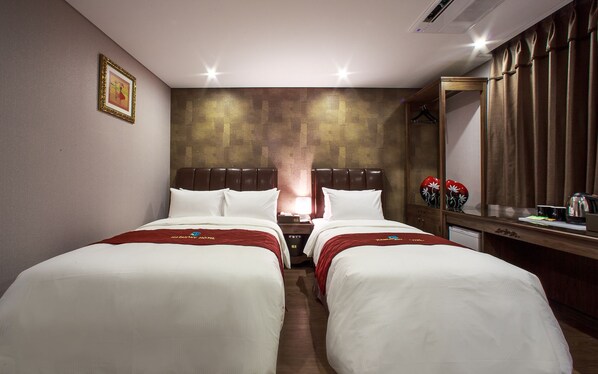 Une chambre d’hôtel avec deux lits, une tête de lit en bois, une table de chevet avec une lampe, un miroir et une armoire.