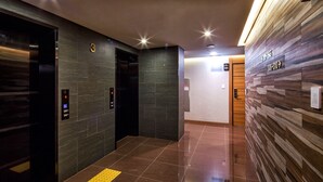 A modern elevator area with digital displays, a tactile paving floor, and a wall with directional signs. - Harmony Hotel (Seoul)