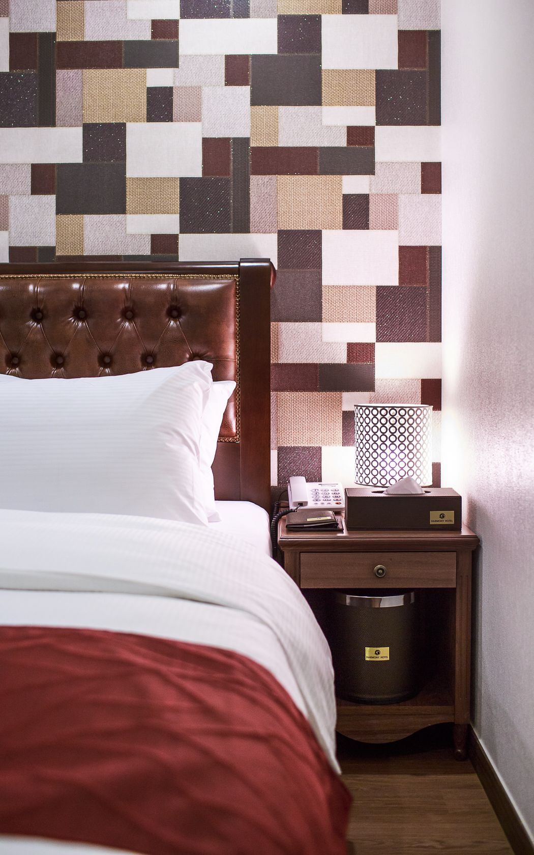 A hotel room with a bed, a nightstand with a lamp, and a wall with a geometric patterned design.