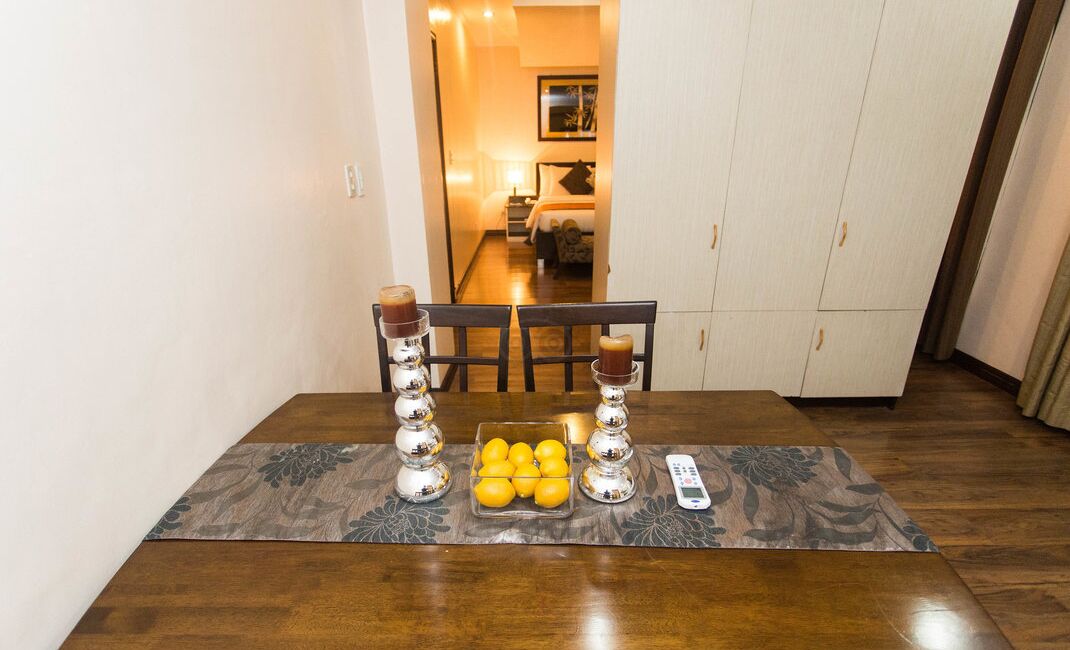 A dining table with a tray of lemons, two decorative candle holders, and a remote control.