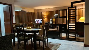 Habitación de hotel con comedor, televisor, sofá y una lámpara decorativa.