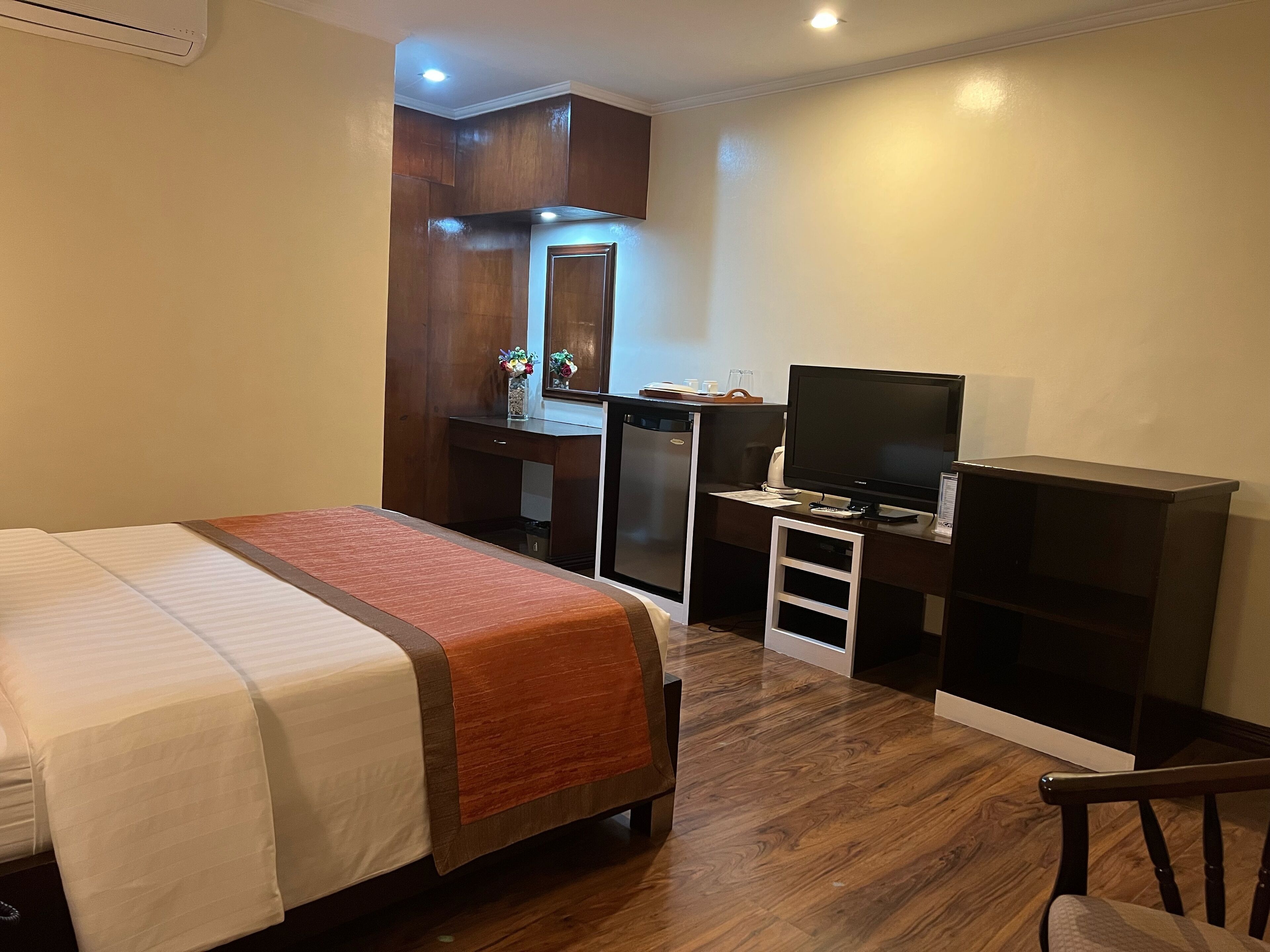 A hotel room with a bed, a desk with a computer, a television, and a small kitchenette.