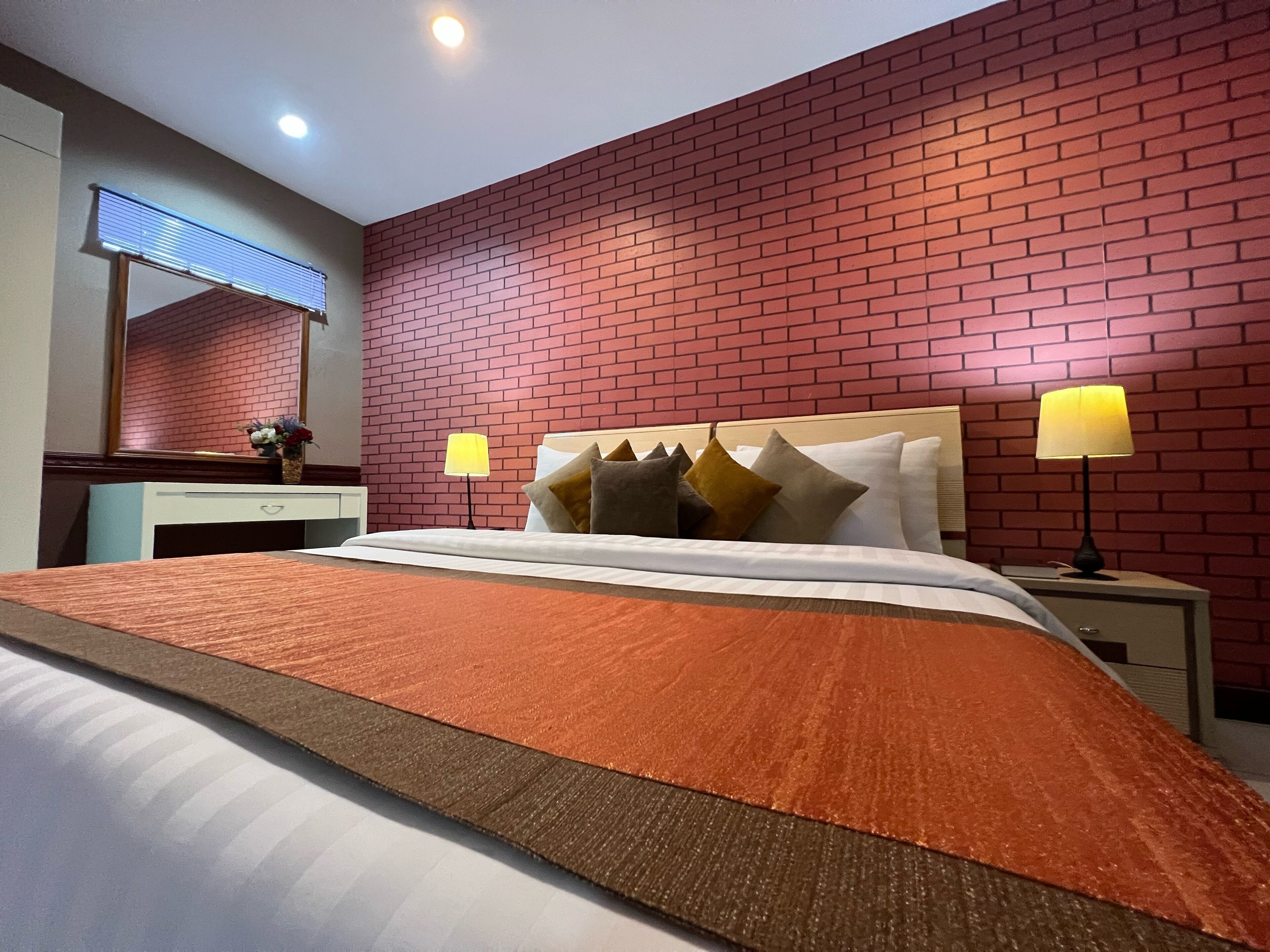 A hotel room with a brick-patterned wall, a bed with white bedding, two bedside lamps, and a nightstand with a lamp.