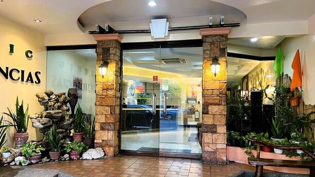 Entrada de hotel con puerta de cristal, pilares de piedra y plantas en macetas.