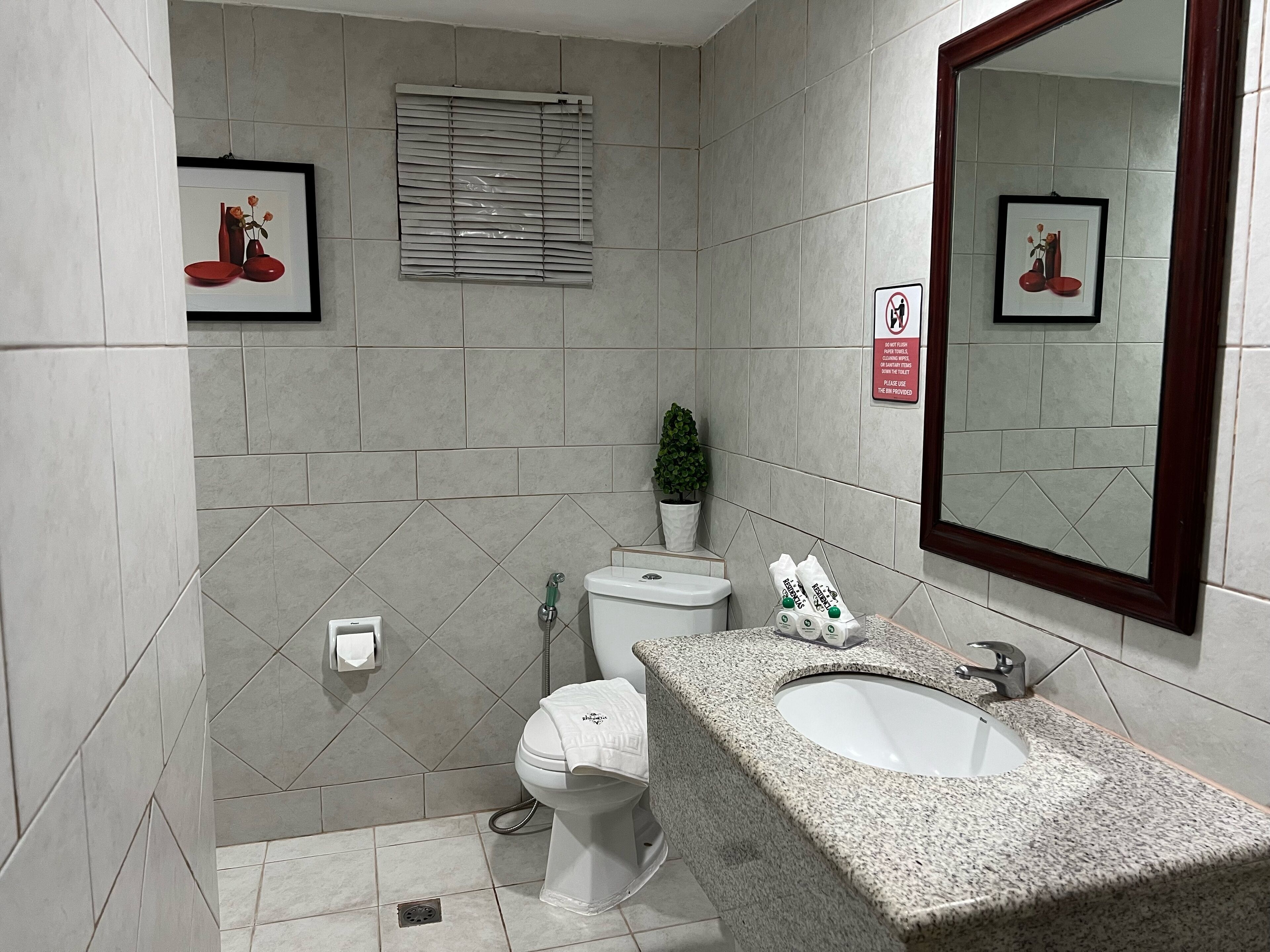 Et badeværelse med toilet, vask og spejl. Væggene er dekoreret med billeder i rammer og der står en potteplante.